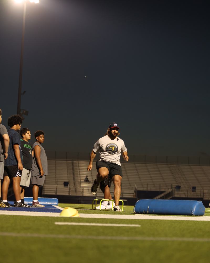 Carl Bradford running a hurdle drill himself while his athletes watch
